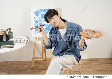 A man in his 20s painting on canvas with paints 120008538