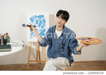 A man in his 20s painting on canvas with paints 120008539