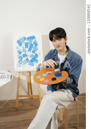 A man in his 20s painting on canvas with paints 120008542