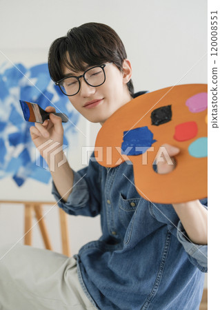 A man in his 20s painting on canvas with paints 120008551