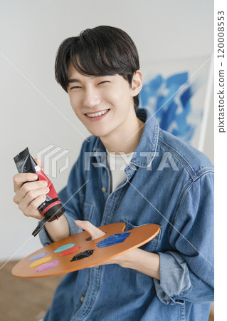 A man in his 20s painting on canvas with paints 120008553