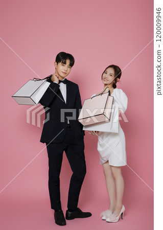 A couple wearing dresses and suits and holding shopping bags A couple wearing dresses and suits and holding shopping bags 120009946