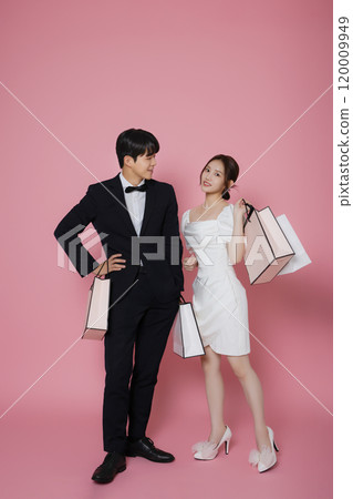 A couple wearing dresses and suits and holding shopping bags 120009949
