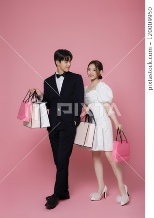 A couple wearing dresses and suits and holding shopping bags 120009950