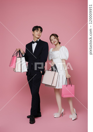 A couple wearing dresses and suits and holding shopping bags A couple wearing dresses and suits and holding shopping bags 120009951