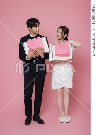 A couple wearing dresses and suits and holding shopping bags 120009956