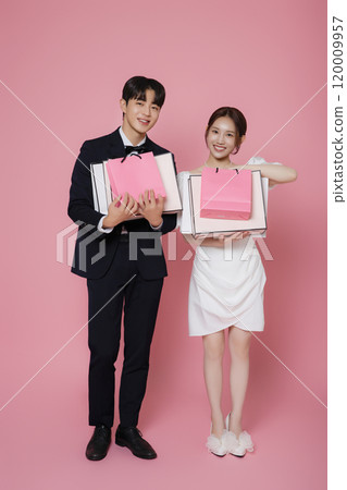 A couple wearing dresses and suits and holding shopping bags 120009957