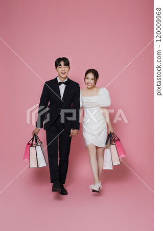A couple wearing dresses and suits and holding shopping bags 120009968