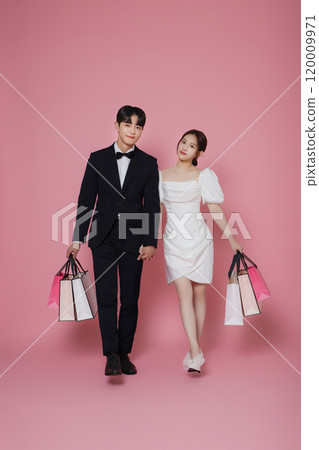 A couple wearing dresses and suits and holding shopping bags A couple wearing dresses and suits and holding shopping bags 120009971