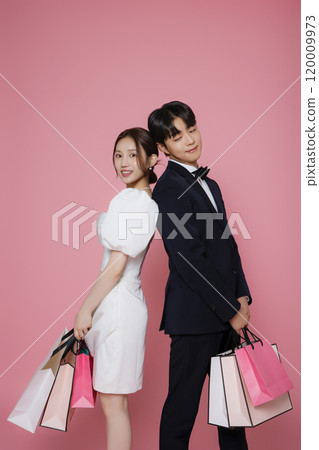 A couple wearing dresses and suits and holding shopping bags 120009973