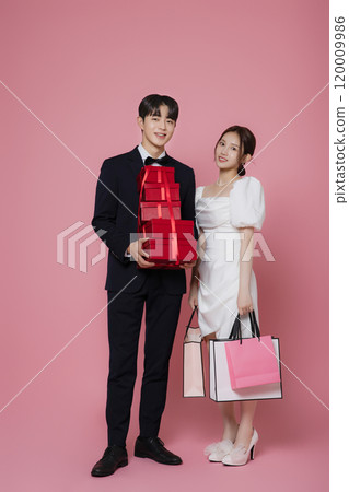 A couple wearing dresses and suits and holding shopping bags 120009986