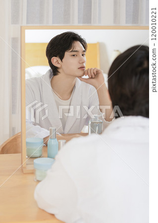 A man in his 20s sitting in front of a mirror and looking at himself for skin care A man in his 20s sitting in front of a mirror and looking at himself for skin care 120010221