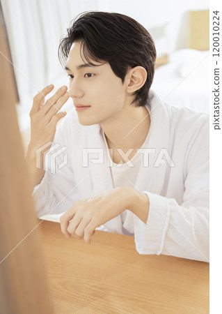 A man in his 20s taking care of his skin while looking in the mirror 120010224