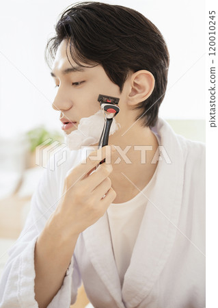 A man in his 20s shaving in front of a mirror 120010245
