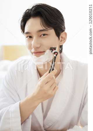 A man in his 20s shaving in front of a mirror 120010251