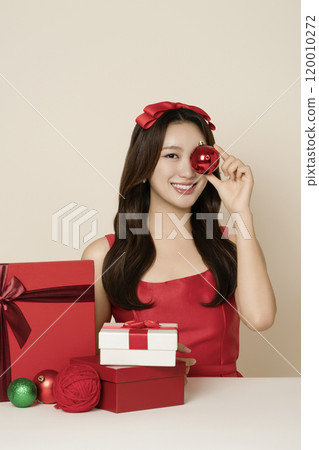 A woman in her 20s wearing a red dress posing with a Christmas ornament 120010272