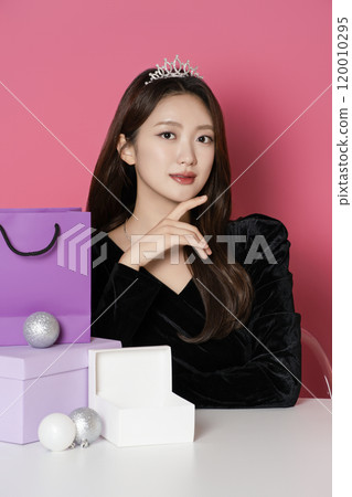 A woman in her 20s wearing a crown and posing in front of a shopping bag and gift box A woman in her 20s wearing a crown and posing in front of a shopping bag and gift box 120010295