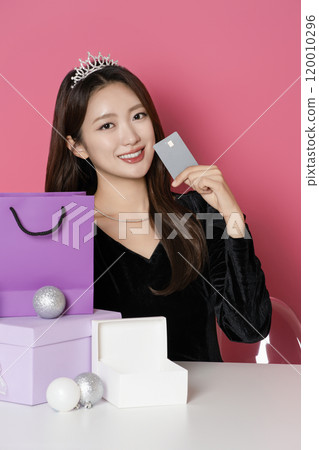 A woman in her 20s wearing a crown and posing in front of a shopping bag and gift box 120010296