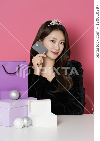 A woman in her 20s wearing a crown and posing in front of a shopping bag and gift box 120010297