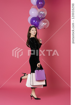 A woman in her 20s wearing a crown and posing with shopping bags and balloons A woman in her 20s wearing a crown and posing with shopping bags and balloons 120010298