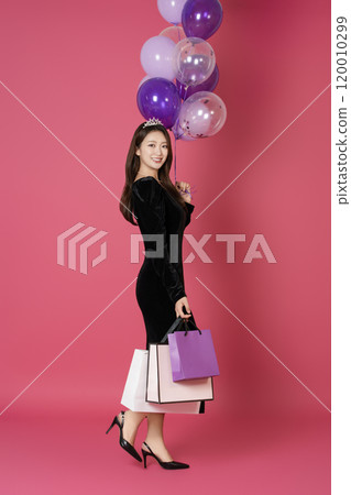 A woman in her 20s wearing a crown and posing with shopping bags and balloons A woman in her 20s wearing a crown and posing with shopping bags and balloons 120010299
