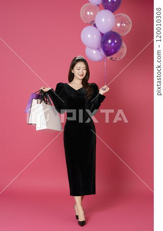 A woman in her 20s wearing a crown and posing with shopping bags and balloons 120010308