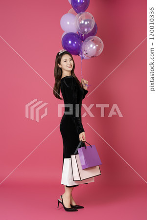 A woman in her 20s wearing a crown and posing with shopping bags and balloons A woman in her 20s wearing a crown and posing with shopping bags and balloons 120010336