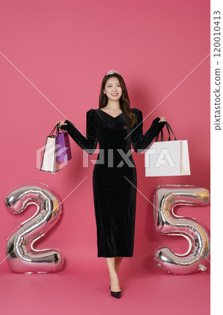 A woman in her 20s posing while holding a shopping bag in front of a 25 number balloon. A woman in her 20s posing while holding a shopping bag in front of a 25 number balloon. 120010413