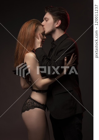 Confident man in black suit kissind a woman on her forehead in dark room Confident man in black suit kissind a woman on her forehead in dark room 120011237