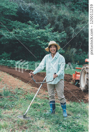 A woman cutting weeds around a field with a brush cutter 120011259