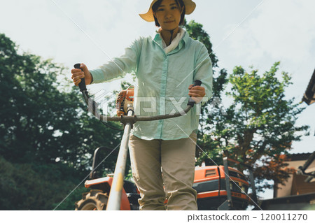 A woman cutting weeds around a field with a brush cutter A woman cutting weeds around a field with a brush cutter 120011270
