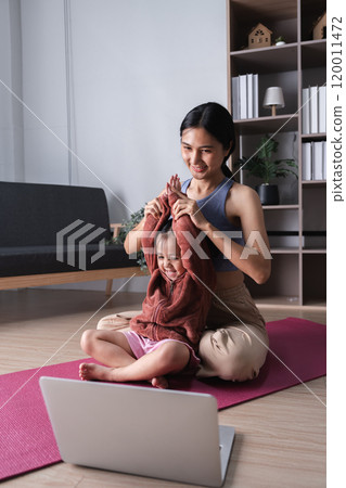 Mother and Child Practicing Yoga Together at Home on a Pink Mat with Laptop in Cozy Living Room Setting 120011472