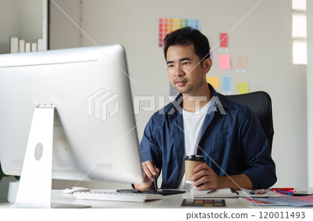 Young Male Graphic Designer Focused on Creative Work at Computer in Modern Office Environment Young Male Graphic Designer Focused on Creative Work at Computer in Modern Office Environment 120011493
