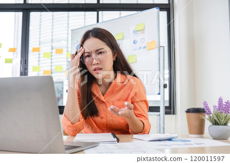 Young Female Accountant Looking Confused While Working on Laptop in Modern Office with Sticky Notes and Documents Young Female Accountant Looking Confused While Working on Laptop in Modern Office with Sticky Notes and Documents 120011597