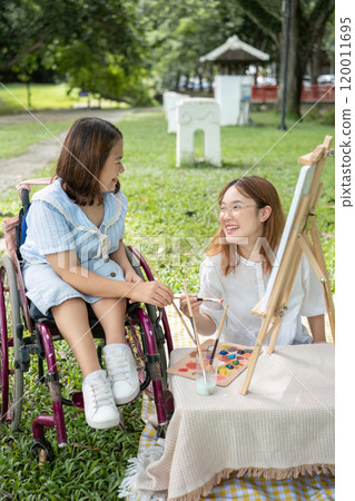 Close Friends, Disabled Young Women Drawing Together Outdoors in a Park, Sharing Creativity and Friendship Close Friends, Disabled Young Women Drawing Together Outdoors in a Park, Sharing Creativity and Friendship 120011695