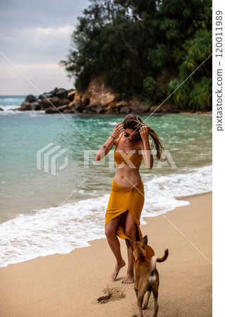 A Young Woman Happily Enjoying a Relaxing Beach Walk with Her Dog by the Ocean Waves 120011989