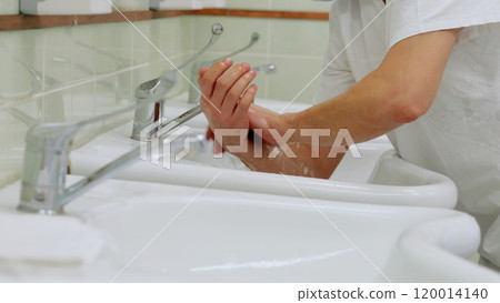 Surgeon meticulously cleans their hands in a hospital restroom before a surgical operation. Emphasizing hygiene is essential for ensuring patient safety in the operating room Surgeon meticulously cleans their hands in a hospital restroom before a surgical operation. Emphasizing hygiene is essential for ensuring patient safety in the operating room 120014140