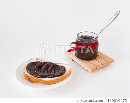 Delicious chocolate spread on bread with jar and red ribbon on white background 120016475