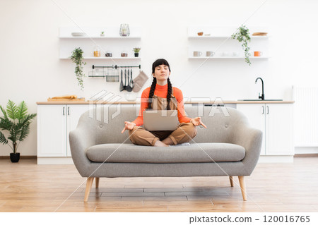 Woman meditating in lotus pose at home during remote work Woman meditating in lotus pose at home during remote work 120016765