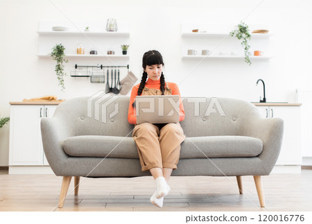 Caucasian woman working remotely on laptop in bright living room Caucasian woman working remotely on laptop in bright living room 120016776