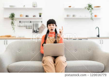 Woman working remotely on laptop from home living room sofa 120016779