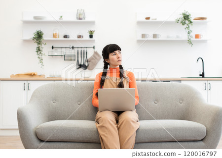 Young woman with laptop sitting on sofa in modern kitchen 120016797