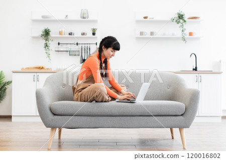 Caucasian woman working remotely on laptop from modern home setting 120016802