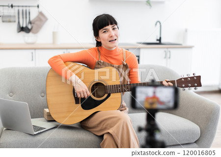 Caucasian woman hosting online guitar lesson from cozy living room Caucasian woman hosting online guitar lesson from cozy living room 120016805