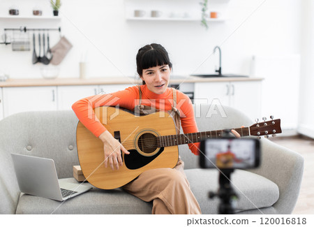 Caucasian female recording guitar tutorial at home with laptop and camera Caucasian female recording guitar tutorial at home with laptop and camera 120016818