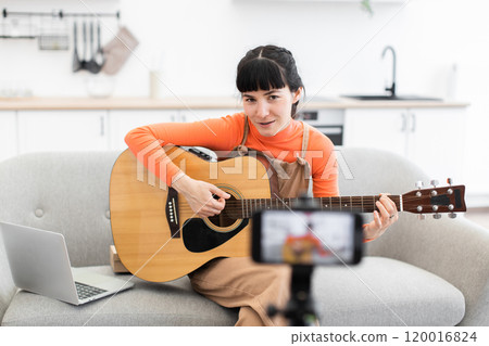 Caucasian female guitarist recording an online lesson at home 120016824