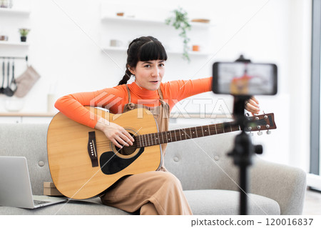 Caucasian female creating online guitar lesson at home on camera Caucasian female creating online guitar lesson at home on camera 120016837