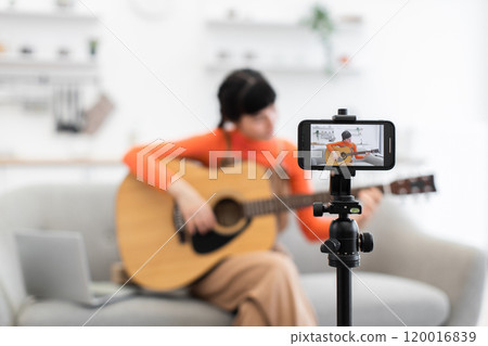 Caucasian woman recording guitar lesson at home for online audience 120016839