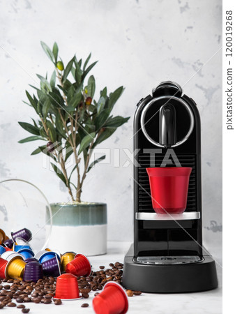Red steel cup with coffee capsules and home espresso machine on white background with fresh aroma coffee beans and plant. Red steel cup with coffee capsules and home espresso machine on white background with fresh aroma coffee beans and plant. 120019268