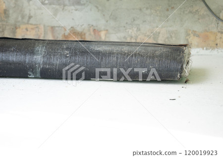 A roll of bituminous roofing material lies on a concrete floor. 120019923